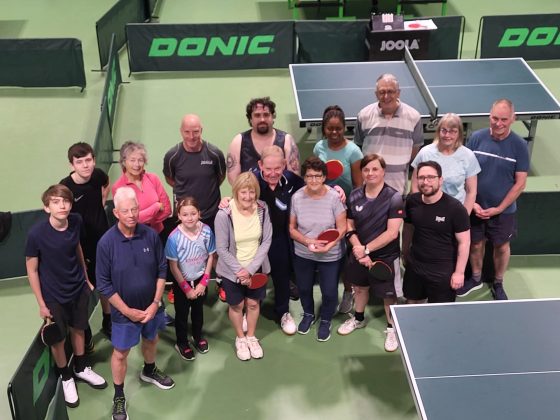 A group of people of different ages stand in a table tennis venue.