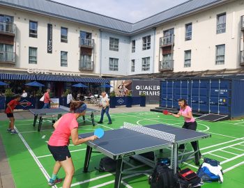 two women play table tennis surrounded by cafes