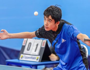 Boy with arms outstretched with a bat in hand looks at the Table Tennis Ball which is in the air in front of his face