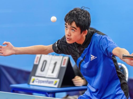 Boy with arms outstretched with a bat in hand looks at the Table Tennis Ball which is in the air in front of his face